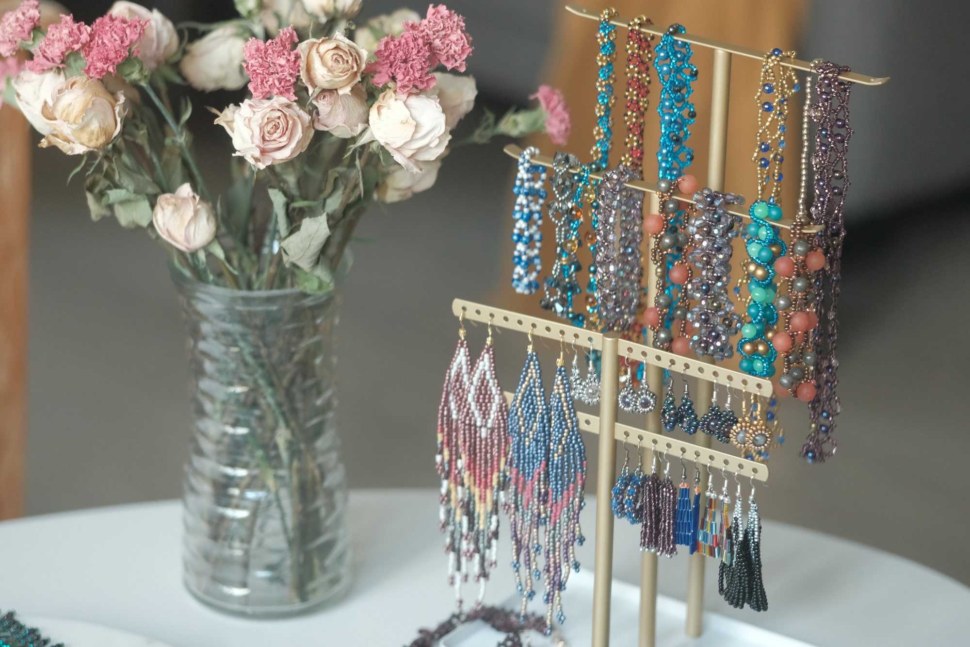 A table of Lynn Germain's beaded jewelry with fresh flowers and a display stand of earrings.